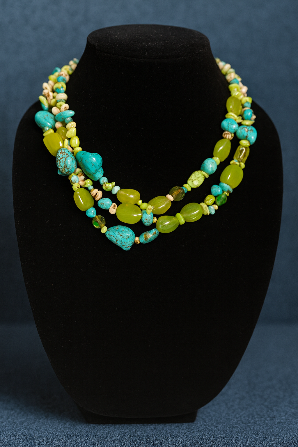 Necklace with turquoise and green beads on a black bust against a blue background